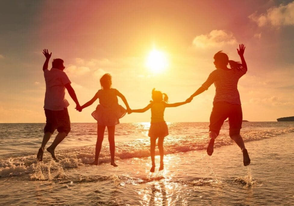 A group of people jumping in the water at sunset.